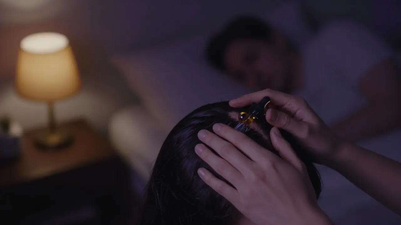 Noční aplikace séra na kůži hlavy pro podporu růstu vlasů, jemné osvětlení a klidná atmosféra.